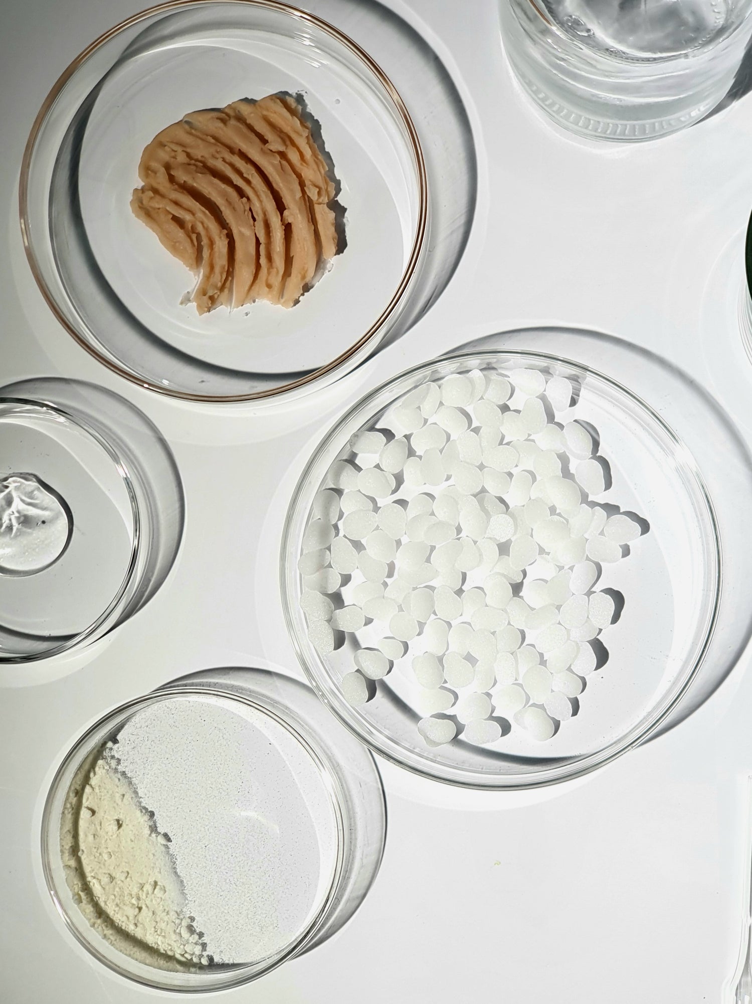 Four petri dishes containing different raw materials for skincare formulation.