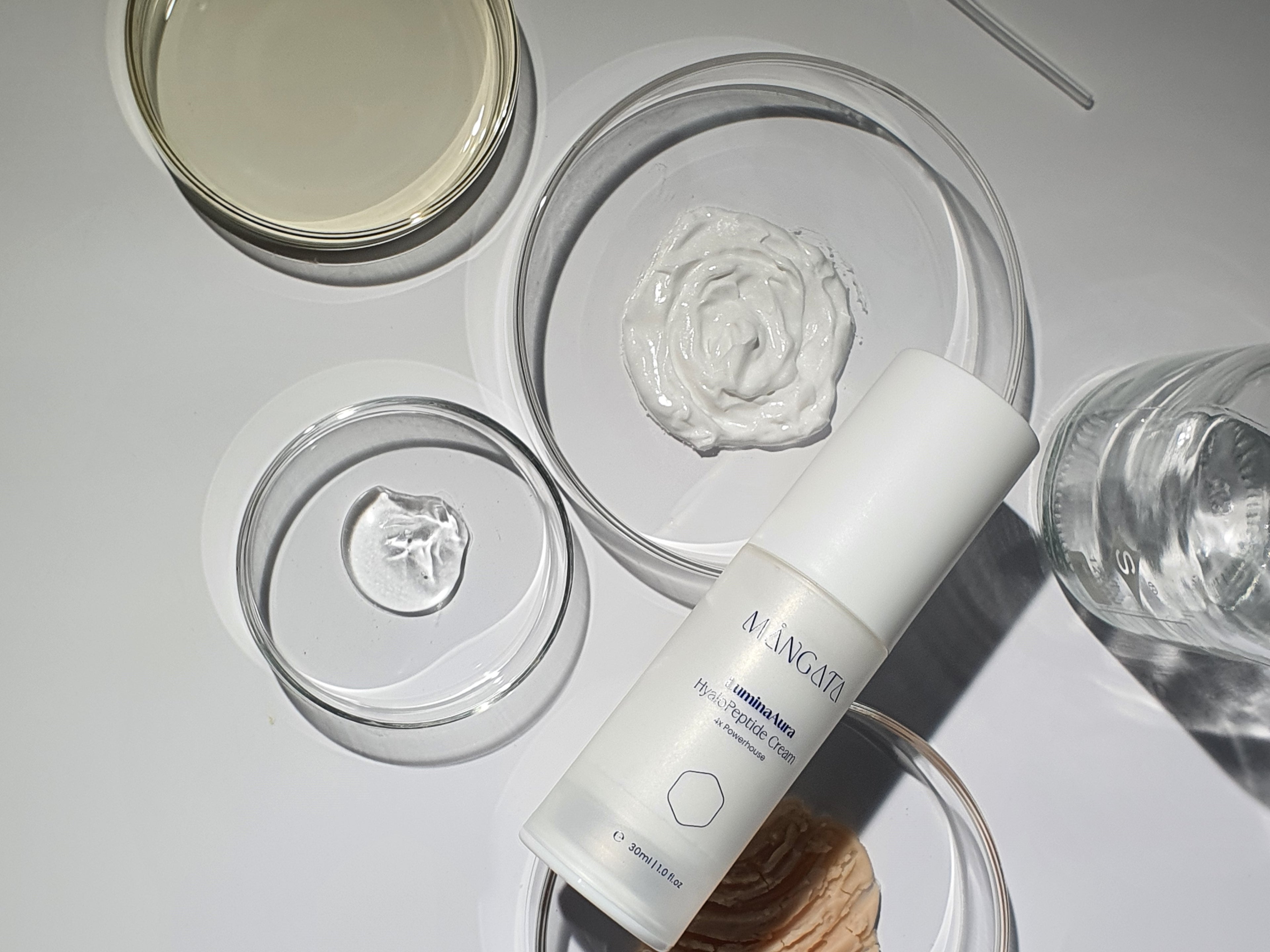 Elegant cream bottle lying on petri dishes filled with various raw materials and natural ingredients.