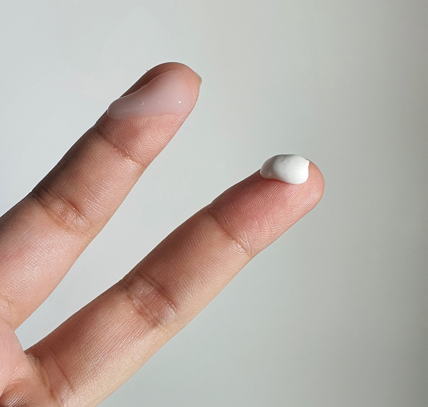 Two fingertips showing opaque skincare essence and velvety white cream respectively.