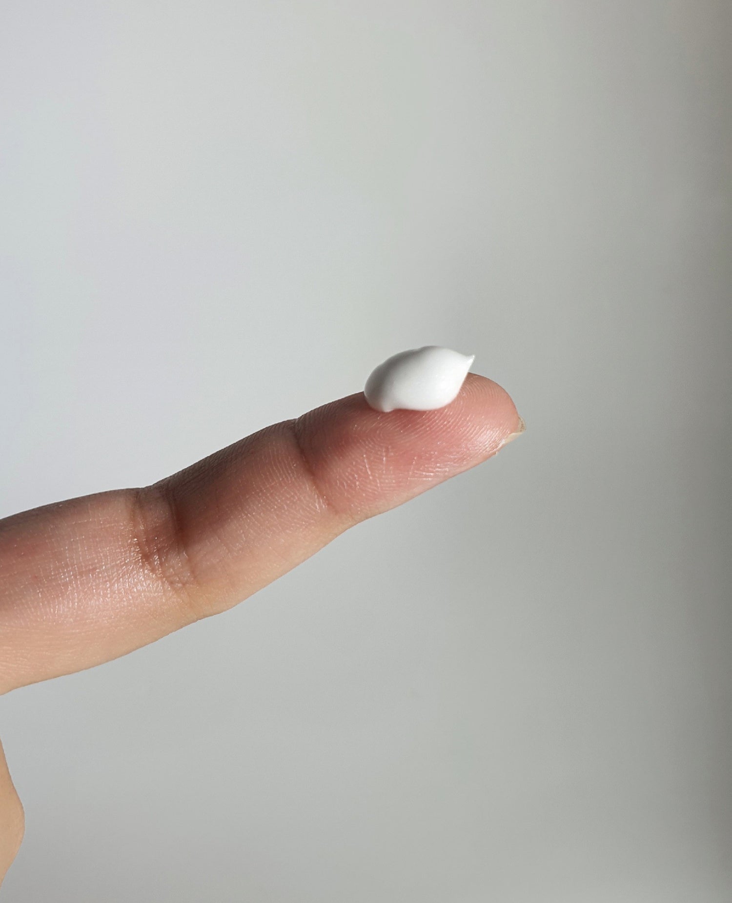 Close-up of fingertip holding a dollop of velvety skin cream, highlighting its rich texture and luxurious feel.