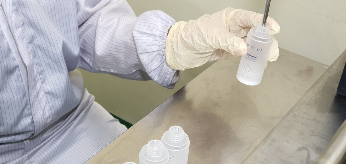 Operator holding a skincare bottle under the filling machine head, ready for it to be filled with product.