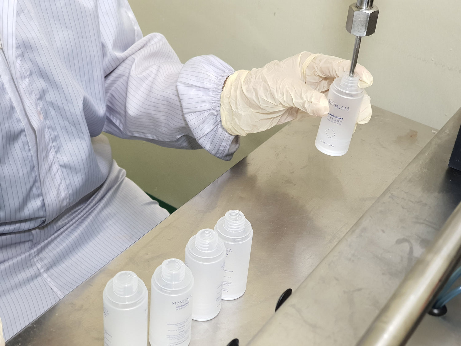 Operator holding a skincare bottle under the filling machine head, ready for it to be filled with product.